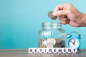 A middle-aged hand placing coins into a piggy bank for their future retirement - they are contributing to their pension for future benefit.