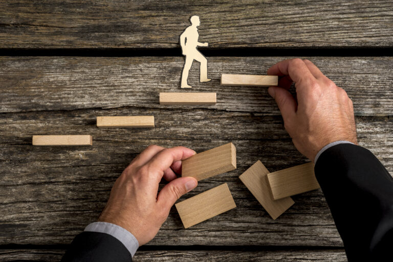 A white male playing with building blocks. The image conceptually visualises a person walking up a flight of stairs, showing his progression and his ability to move forward.